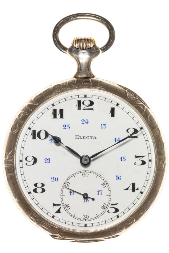 Montre de poche ou à gousset en argent du tir cantonal vaudois à Bex en 1922. Cette montre de poche, disponible lors de cet événement est une pièce commémorative fabriquée à Chaux-de-Fonds par "Electa" (ELECTA GALLET & Co), nom inscrit en noir sur son cadran en émail blanc. Les aiguilles en acier ainsi que les chiffres des heures sont noirs avec un indicateur des 24 heures en bleu. Elle dispose d'un sous-cadran pour les secondes sur la partie inférieure. La lunette en métal est gravée avec l'inscription "Tir Cantonal Vaudois Bex 1922"